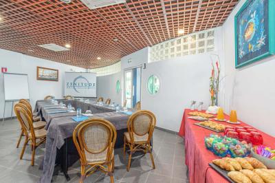 Chambre lumineuse avec lit double, mobilier en bois, télévision et balcon offrant une vue sur des palmiers.