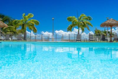 Chambre lumineuse avec lit double, mobilier en bois, télévision et balcon offrant une vue sur des palmiers.