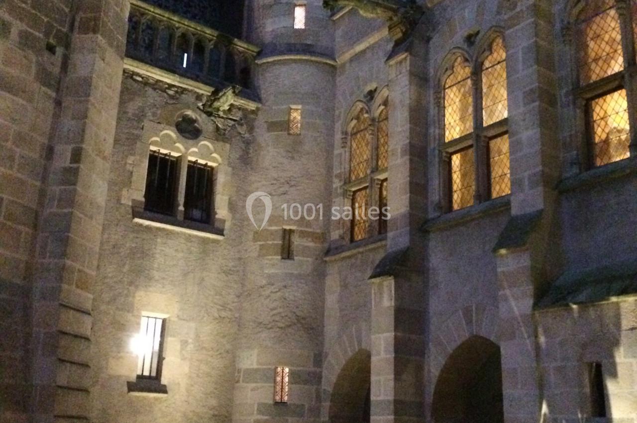 Cour intérieure d'un château en pierre éclairée à la tombée de la nuit, avec un brasero allumé au premier plan.