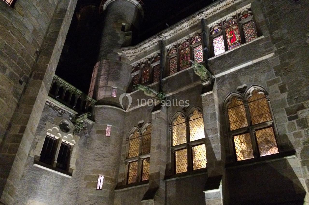 Façade d'un bâtiment ancien en pierre avec des fenêtres illuminées et des vitraux, vue de nuit.