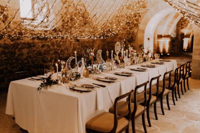 Grande table dressée en extérieur avec vaisselle, décorations florales et citrons, entourée de chaises en bois.
