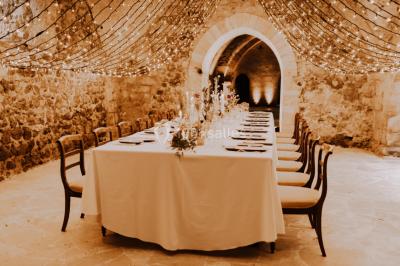 Grande table dressée en extérieur avec vaisselle, décorations florales et citrons, entourée de chaises en bois.
