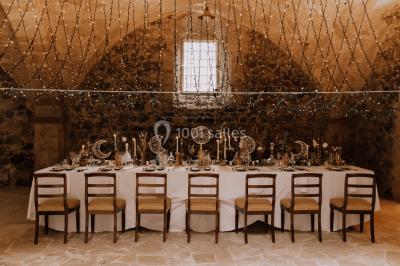 Grande table dressée en extérieur avec vaisselle, décorations florales et citrons, entourée de chaises en bois.