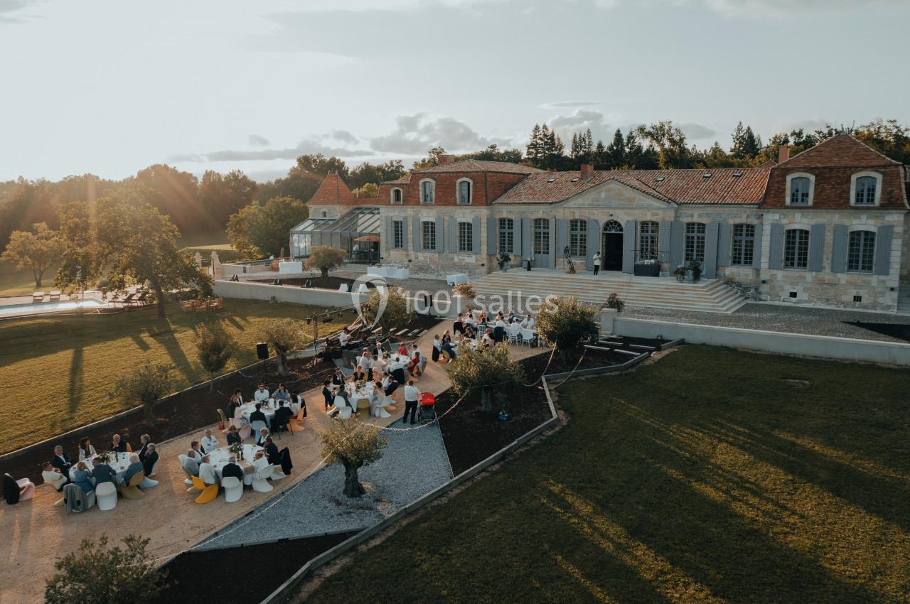 Vue aérienne d'un domaine avec une grande bâtisse en pierre et des invités assis à des tables en extérieur.