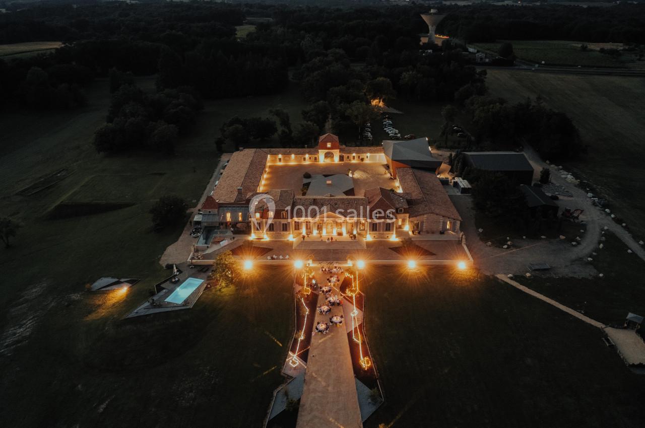 Vue aérienne d'un domaine éclairé de nuit avec une allée illuminée menant à un bâtiment principal entouré de verdure.