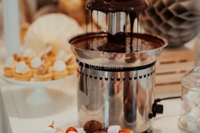 Grande table dressée en extérieur avec vaisselle, décorations florales et citrons, entourée de chaises en bois.