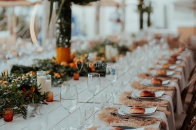 Grande table dressée en extérieur avec vaisselle, décorations florales et citrons, entourée de chaises en bois.