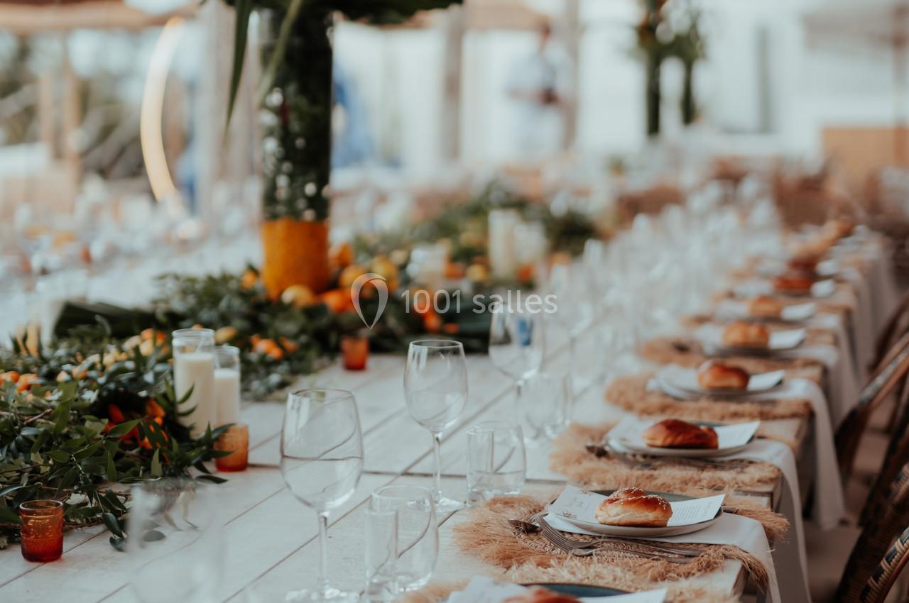 Table élégamment dressée avec des assiettes, des verres et une décoration florale tropicale dans un cadre extérieur.