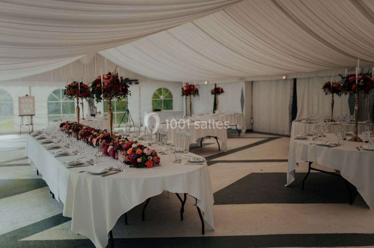 Salle de réception sous chapiteau avec tables décorées de nappes blanches et arrangements floraux colorés.