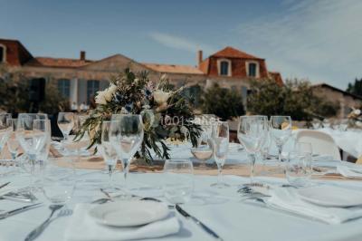 Grande table dressée en extérieur avec vaisselle, décorations florales et citrons, entourée de chaises en bois.