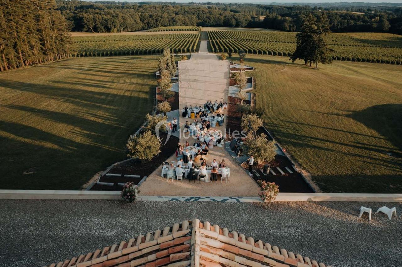Vue aérienne d'une cérémonie en plein air avec des invités assis, entourée de vignes et d'espaces verts.