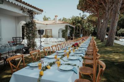 Grande table dressée en extérieur avec vaisselle, décorations florales et citrons, entourée de chaises en bois.