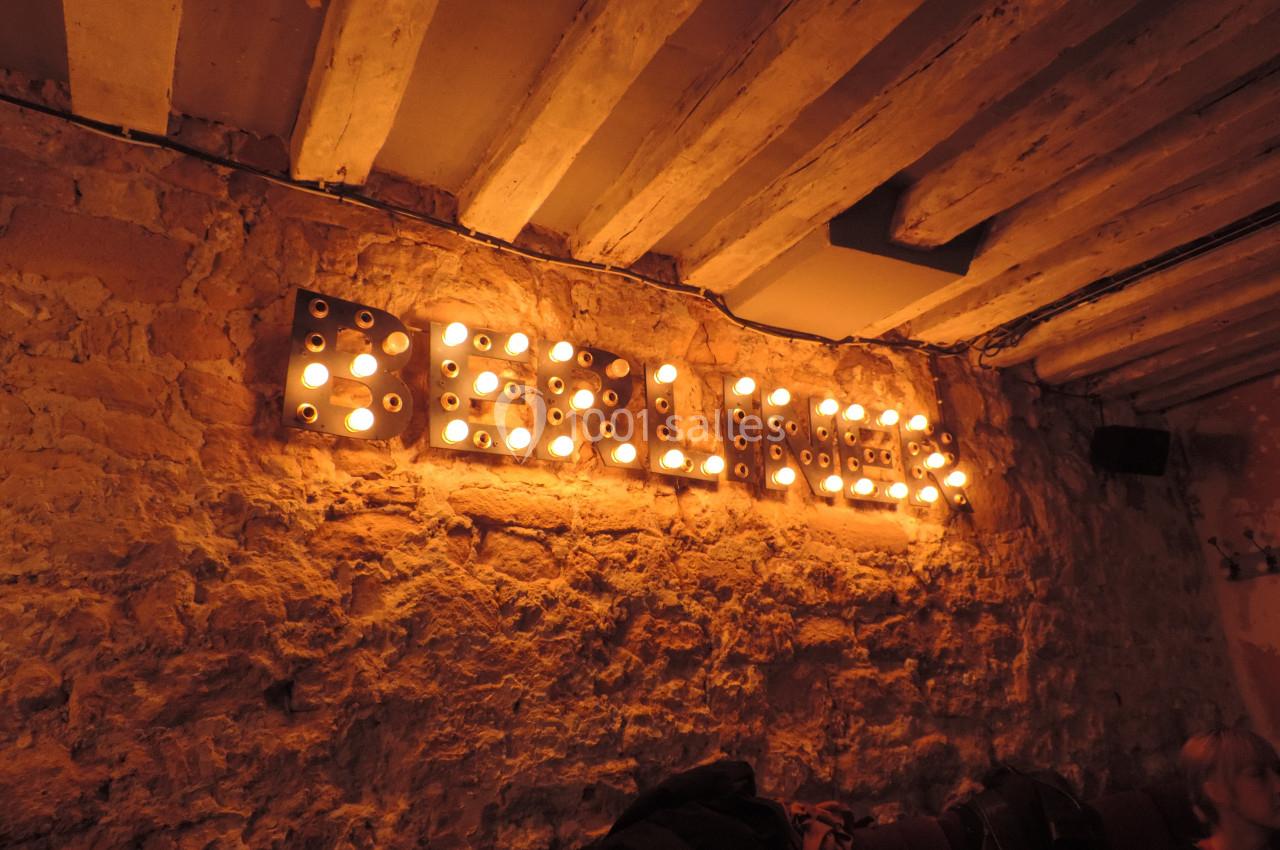 Enseigne lumineuse ’Berlin’ fixée sur un mur en pierre dans un intérieur à l'éclairage tamisé.