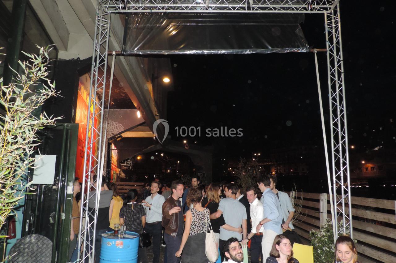Groupe de personnes discutant sur une terrasse extérieure éclairée, près d'un fleuve, en soirée.