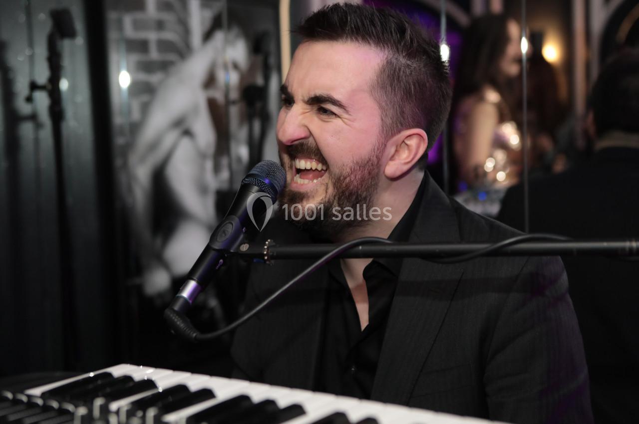Un homme chante en jouant du clavier dans un environnement intérieur avec un micro devant lui.