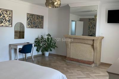 Salle lumineuse avec tables rectangulaires, chaises noires et verrerie suspendue, donnant sur de grandes fenêtres.