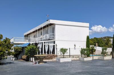 Salle lumineuse avec tables rectangulaires, chaises noires et verrerie suspendue, donnant sur de grandes fenêtres.
