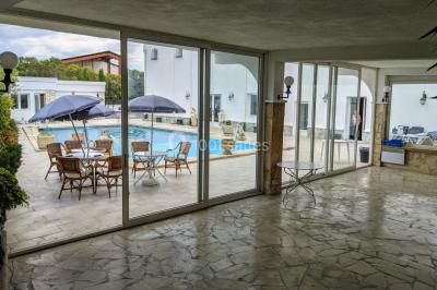 Salle lumineuse avec tables rectangulaires, chaises noires et verrerie suspendue, donnant sur de grandes fenêtres.