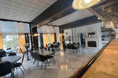 Salle lumineuse avec tables rectangulaires, chaises noires et verrerie suspendue, donnant sur de grandes fenêtres.