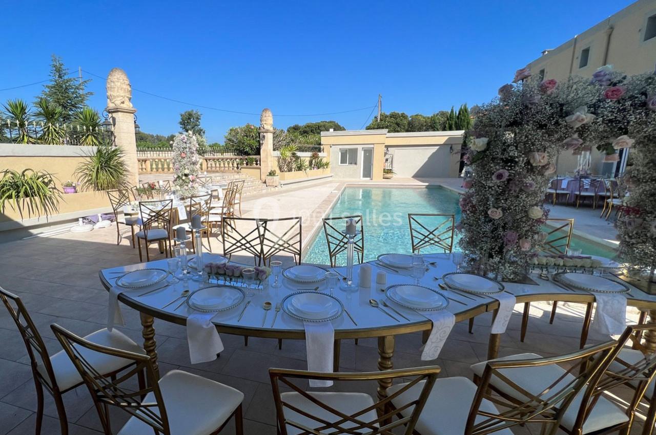 Table élégamment dressée en extérieur près d'une piscine, entourée de décorations florales et de chaises dorées.