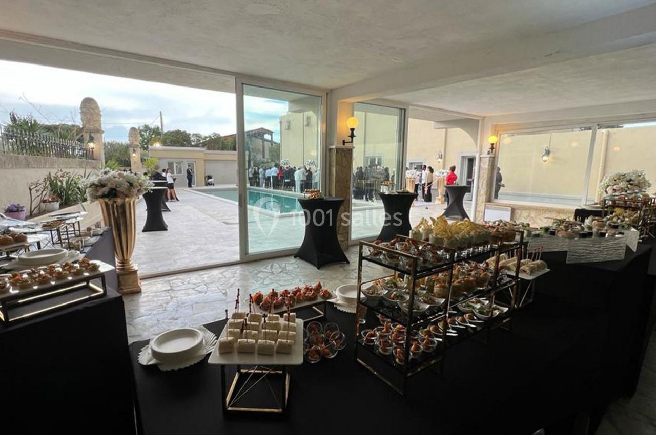 Buffet de réception avec amuse-bouches variés, installé près d'une piscine et d'une salle vitrée lumineuse.