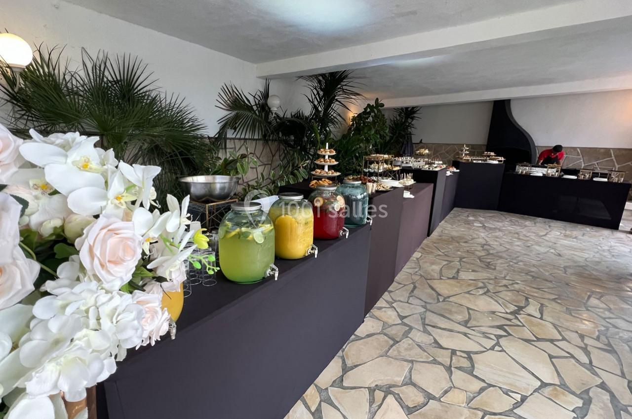 Buffet avec boissons colorées en jarres, fleurs blanches en premier plan et décor végétal en arrière-plan.
