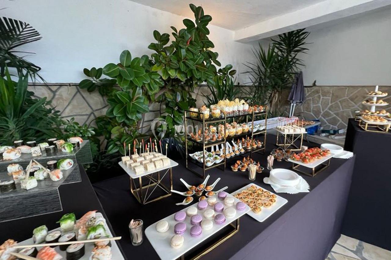 Buffet élégant avec une variété de bouchées salées, desserts et sushis, présenté sur des tables noires décorées de plantes.