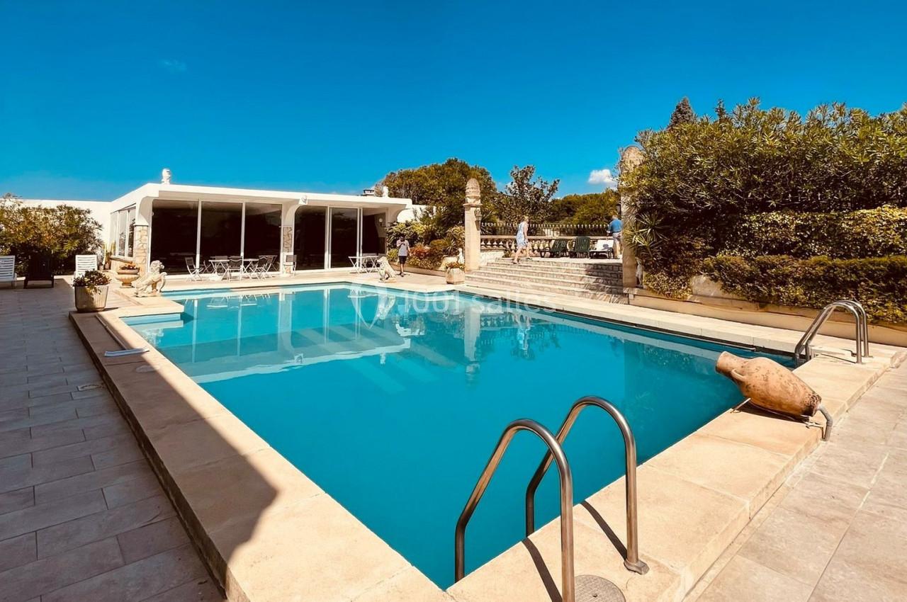 Piscine extérieure entourée de végétation et d'une terrasse en pierre, avec un bâtiment moderne en arrière-plan.