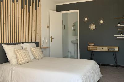 Chambre lumineuse avec lit double, décoration murale en bois et accès à une salle de bain attenante.