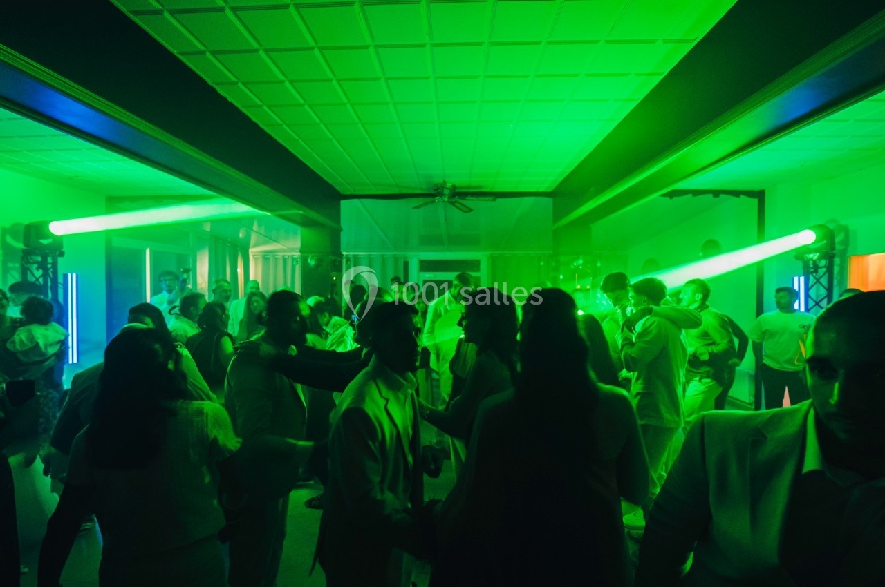 Personnes dansant dans une salle éclairée par des lumières vertes, ambiance festive et animée.