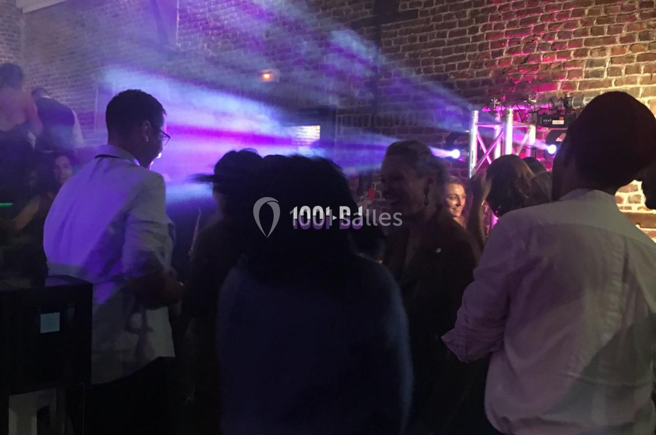 Groupe de personnes dans une ambiance festive avec jeux de lumière colorés dans une salle en briques apparentes.