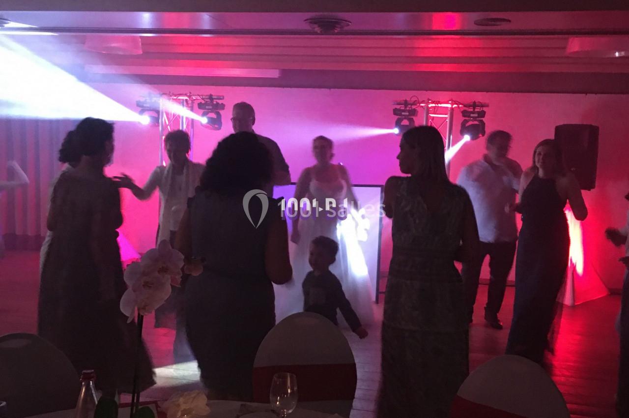 Des personnes dansent dans une salle faiblement éclairée avec des lumières colorées et une table dressée au premier plan.