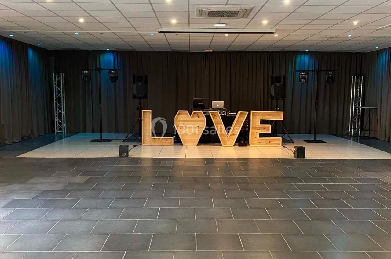 Scène décorée avec des lettres lumineuses formant le mot ’LOVE’, entourée de rideaux et d'équipements audio.