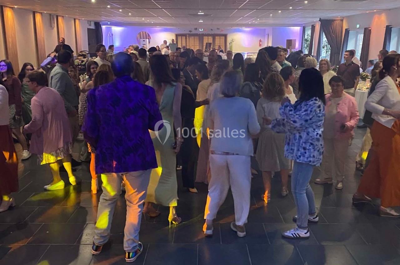 Des personnes dansent dans une salle éclairée, entourées de convives lors d’un événement festif.