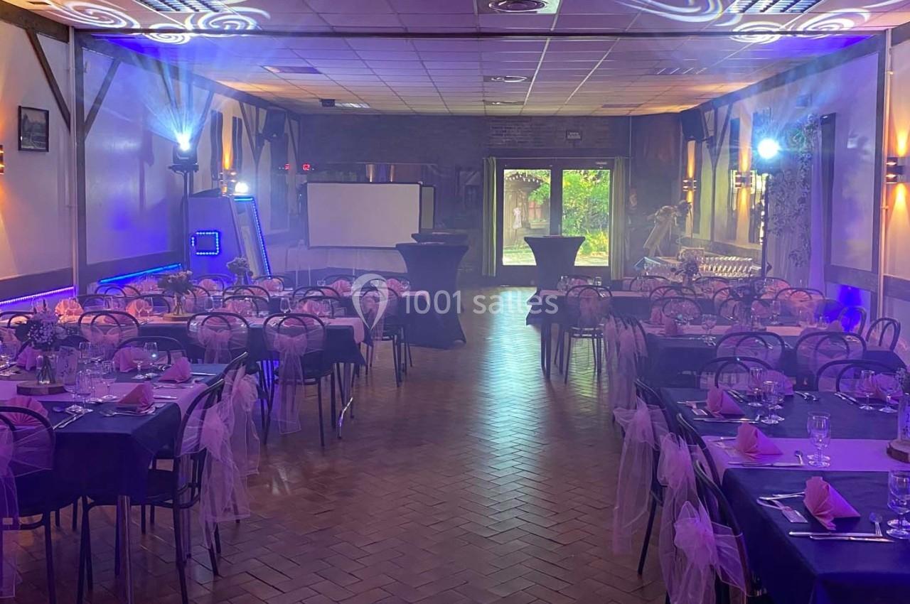 Salle de réception décorée avec des tables dressées, éclairages colorés et ambiance festive.