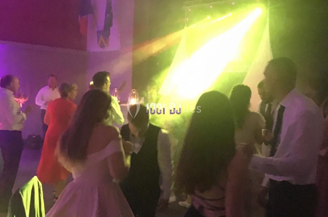 Des personnes dansent dans une salle éclairée par des lumières colorées, avec un DJ en arrière-plan.