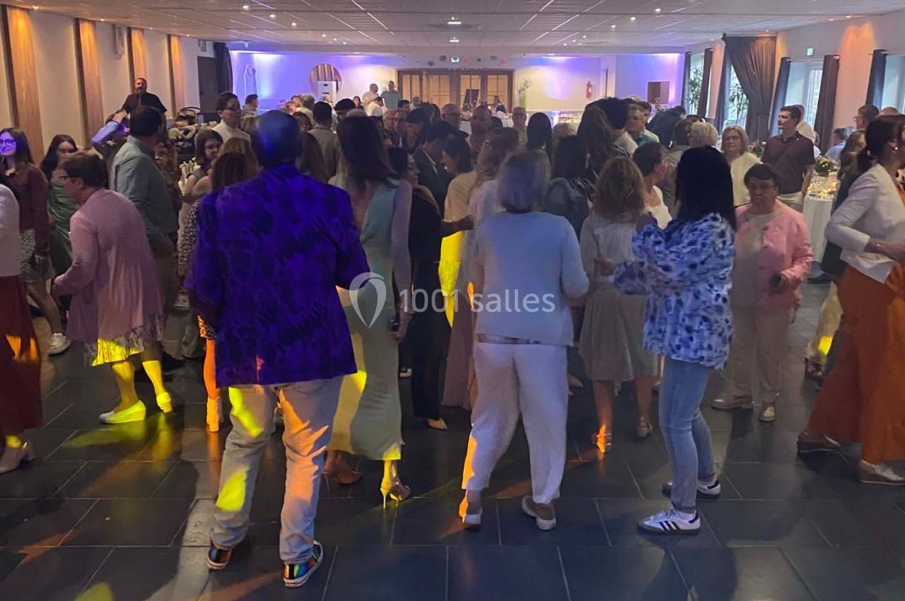 Des personnes dansent dans une salle éclairée par des lumières colorées, lors d'un événement festif.