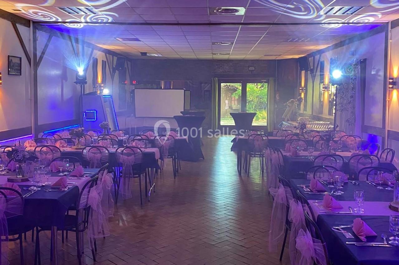 Salle de réception décorée avec des tables dressées, nappes roses et éclairages d'ambiance violets.