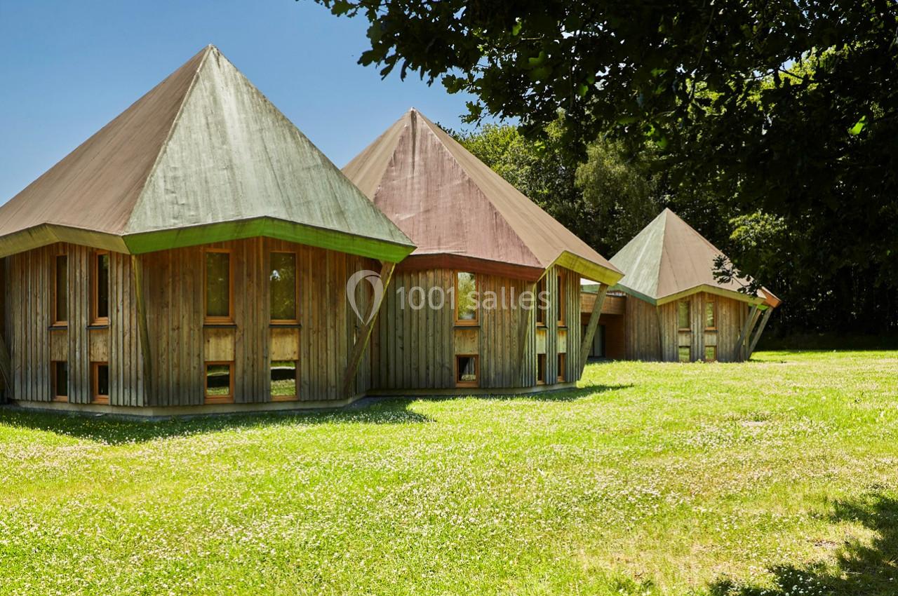 Trois cabanes en bois à toits pointus, situées sur une pelouse verdoyante entourée d'arbres.