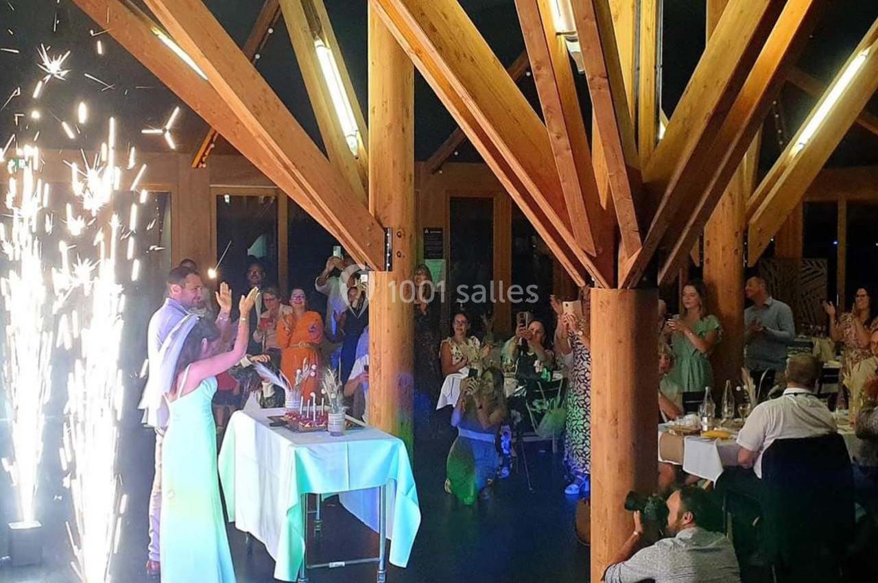 Un couple danse sous des étincelles dans une salle en bois, entouré d'invités assis et debout.