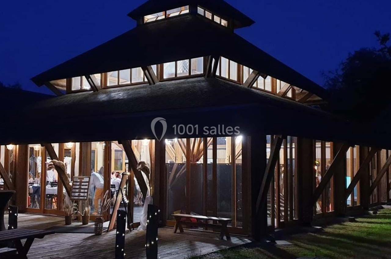 Bâtiment en bois avec de grandes baies vitrées éclairé de l'intérieur, entouré d'herbe et photographié de nuit.