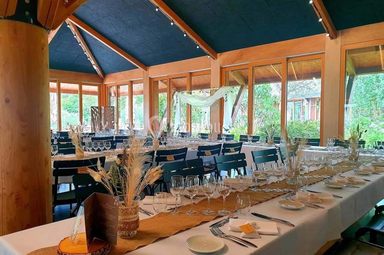 Salle de réception lumineuse avec grandes baies vitrées, tables dressées élégamment et décoration naturelle.