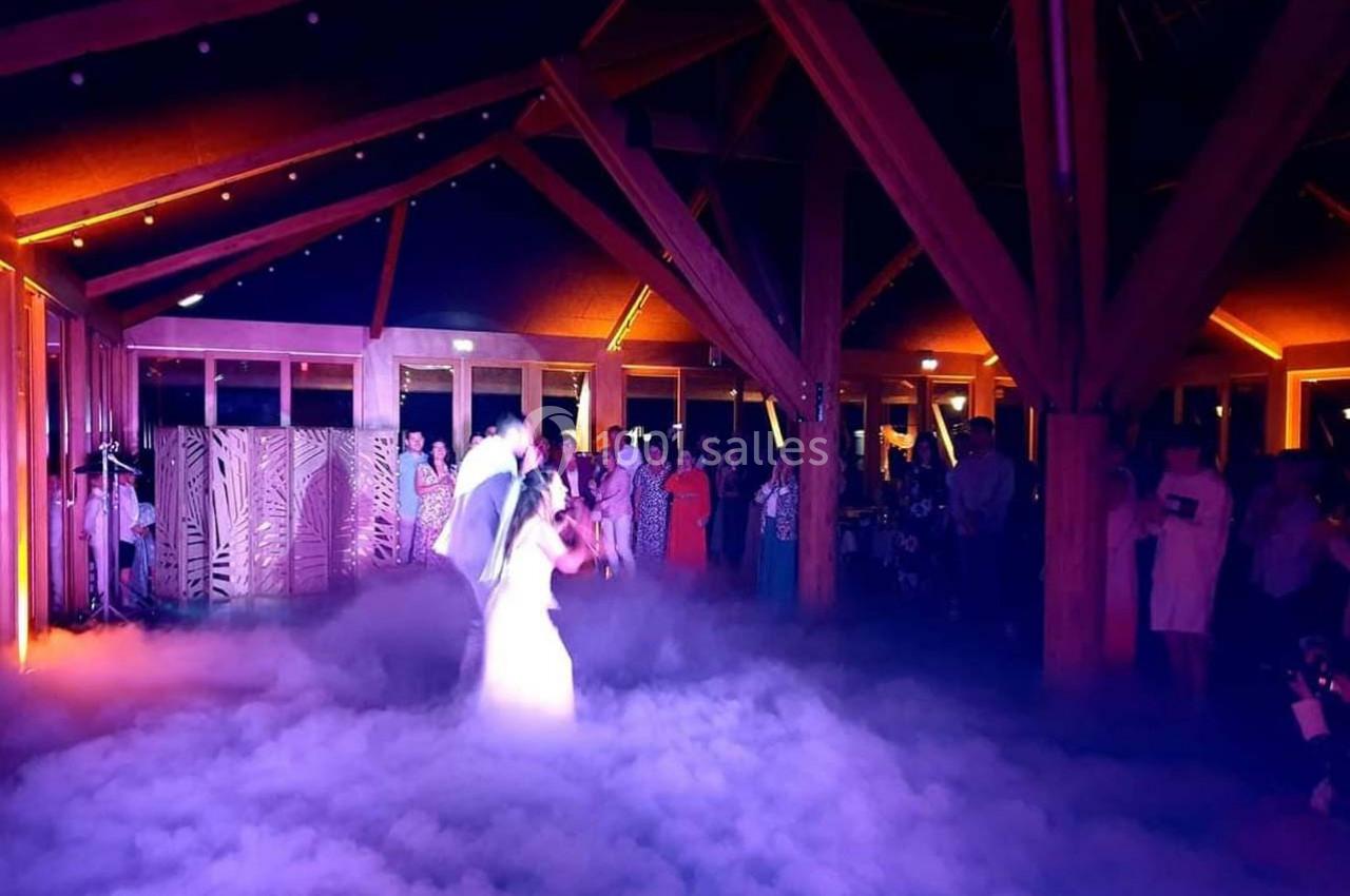 Un couple danse au milieu d'une salle éclairée, entouré d'un effet de fumée au sol et d'invités en arrière-plan.