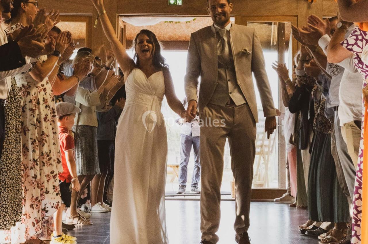 Un couple de mariés souriant entre dans une salle, entouré d'invités applaudissant.