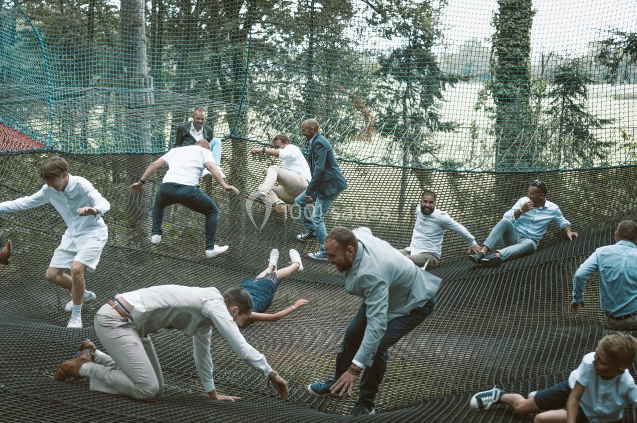 Des personnes de tous âges jouent et se déplacent sur un grand filet suspendu en extérieur, entouré d'arbres.
