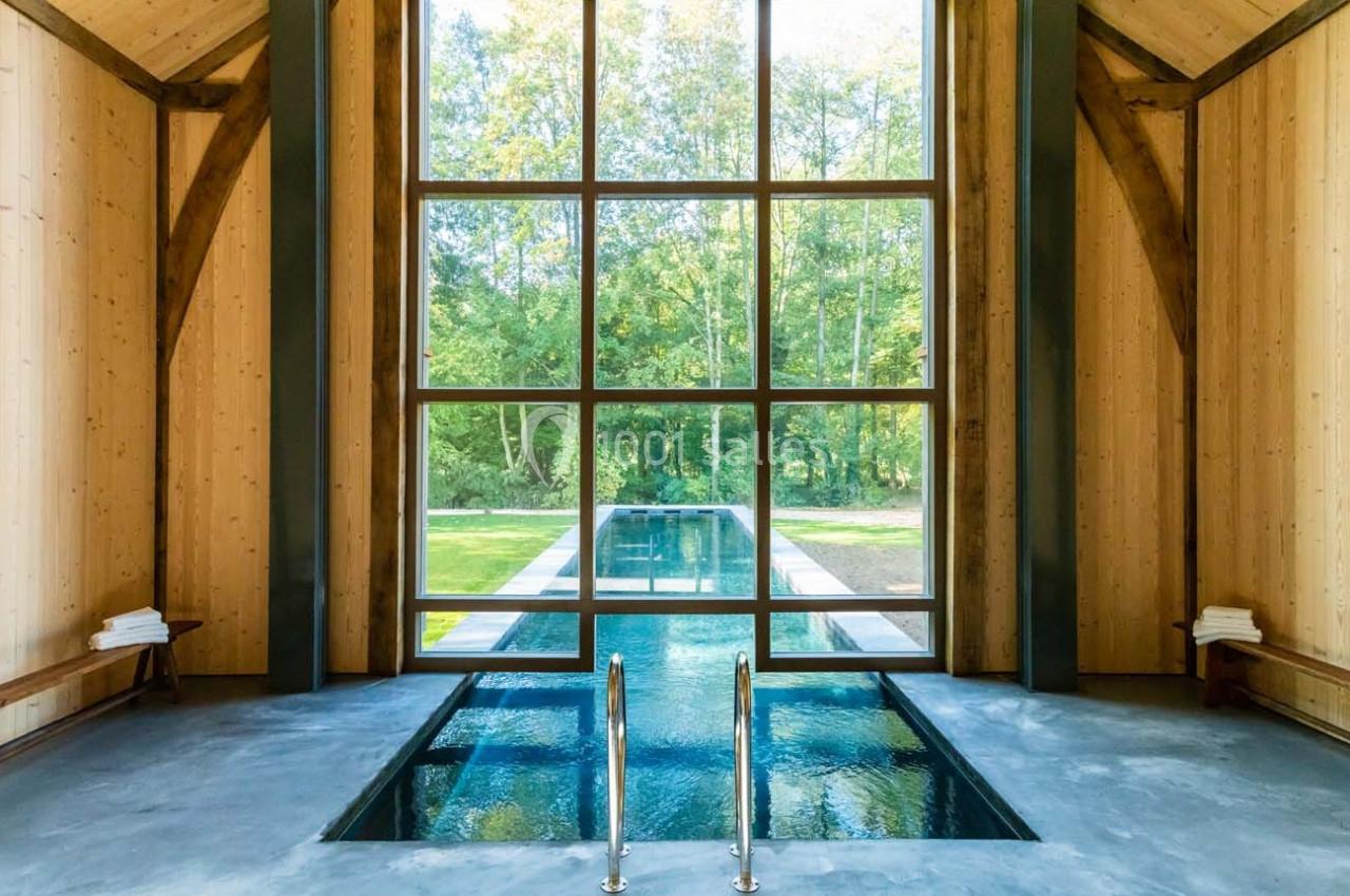 Piscine intérieure avec baies vitrées donnant sur un jardin verdoyant, entourée de murs en bois clair.