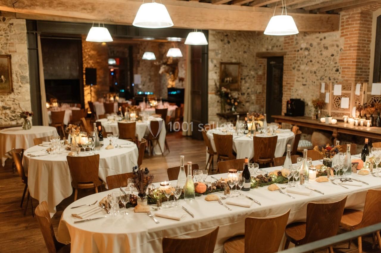 Salle de réception chaleureuse avec tables décorées pour un dîner, éclairage doux et ambiance conviviale.