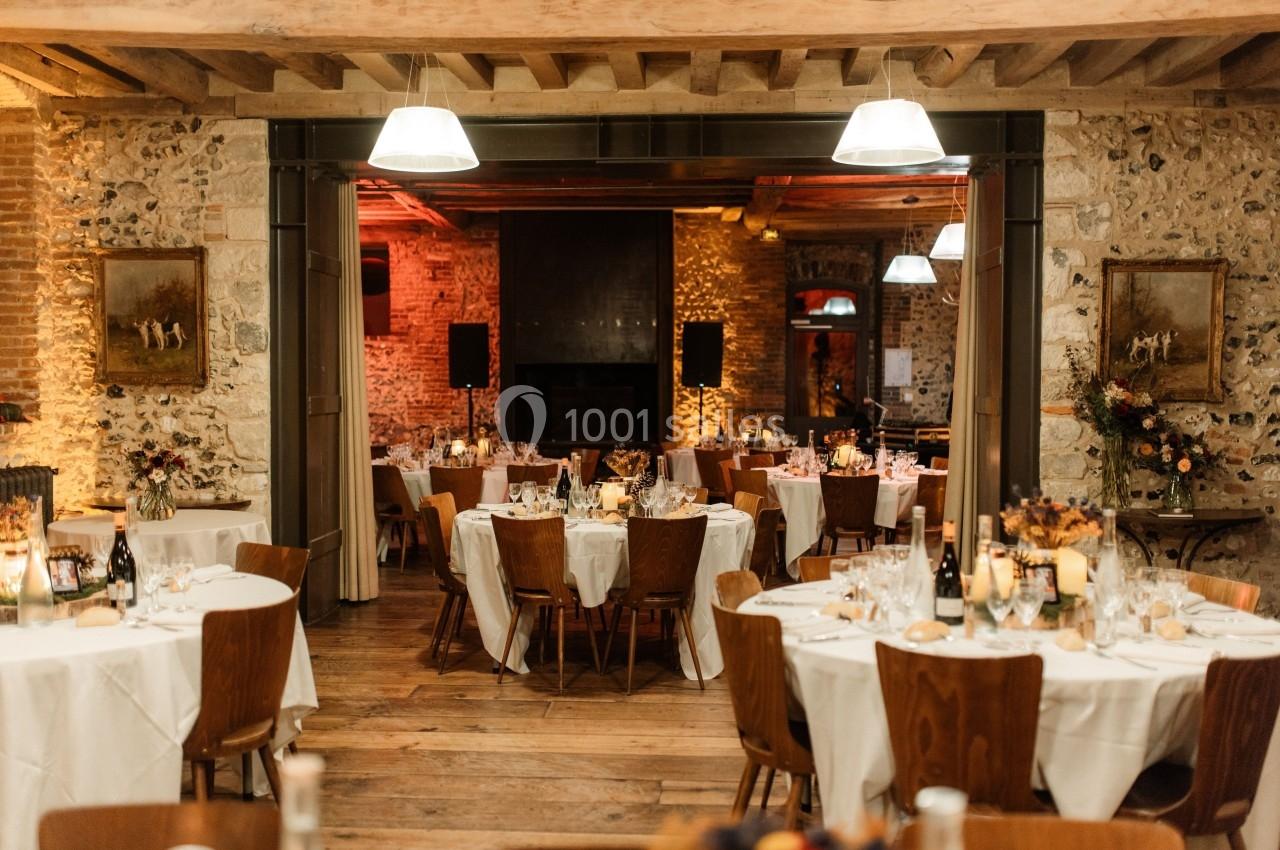 Salle de réception chaleureuse avec tables dressées, éclairage tamisé et murs en pierre apparente.