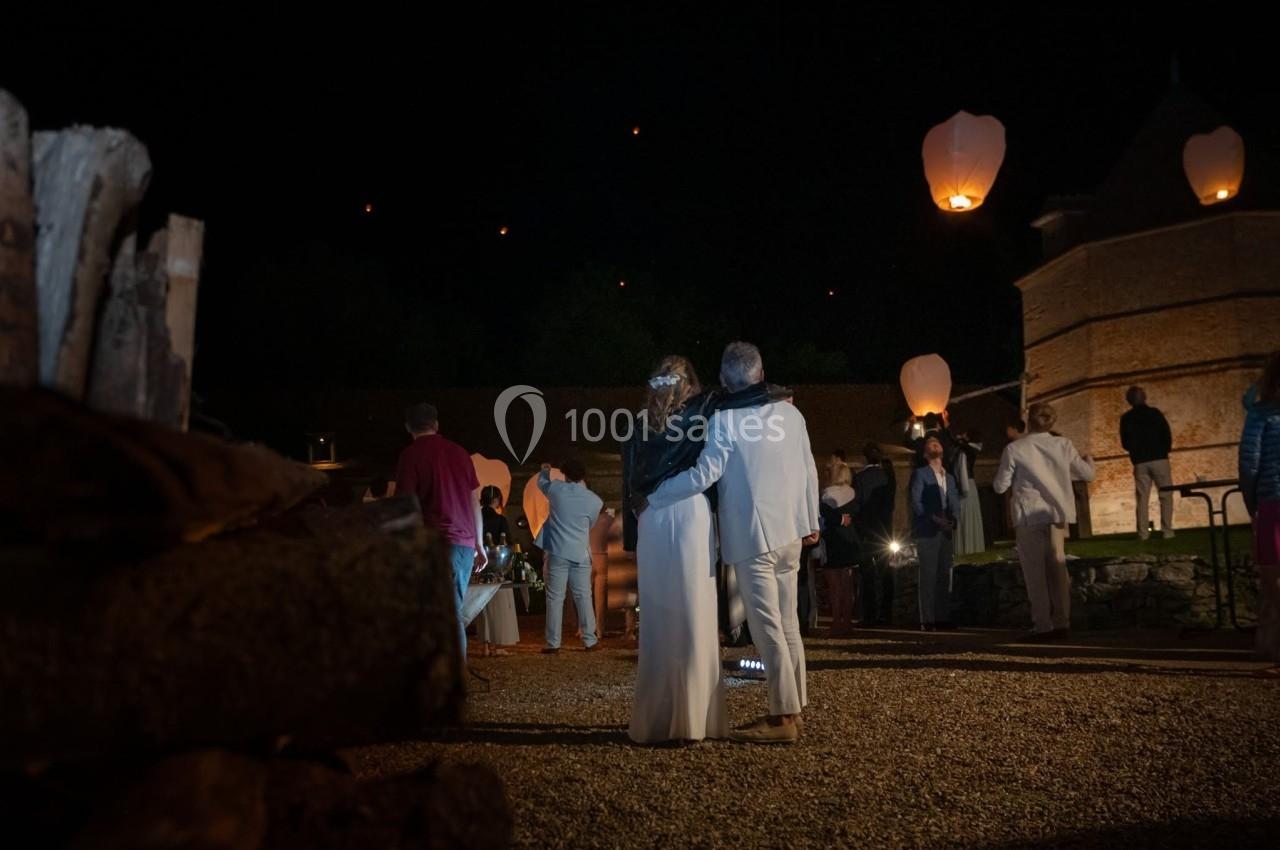 Un couple de dos observe des lanternes volantes dans un cadre nocturne entouré de convives.