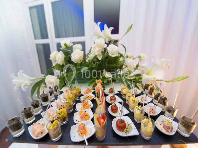 Plateau de verrines et amuse-bouches variés disposés devant un bouquet de fleurs blanches.